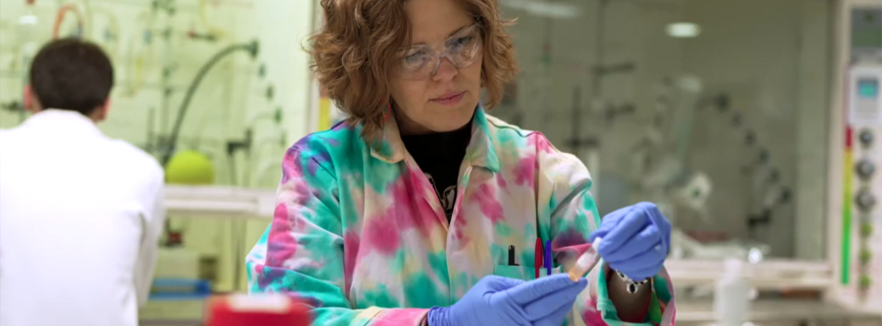 A researcher wearing safety glasses and colourful lab coat examines a sample in an Oxford Chemistry laboratory.