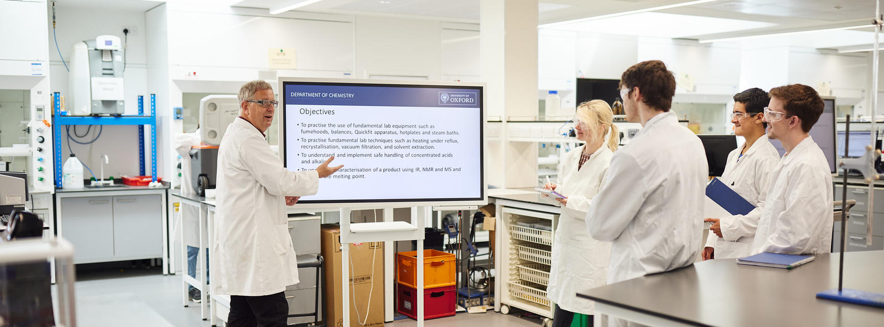 Students in labcoats listening to a presentation in the teaching labs.