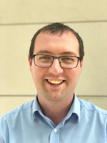 Headshot photo of Andrew Frawley, wearing glasses and a light blue shirt.