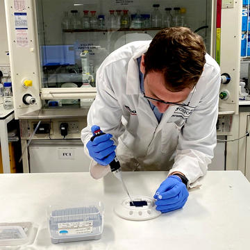 A researcher in a white lab coat pipettes a sample.