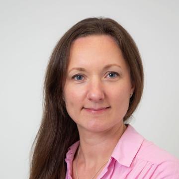 A portrait photograph of a woman with shoulder length brown hair wearing a pink blouse.