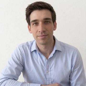 A portrait photo of a man with short dark hair wearing an open-collared white shirt.