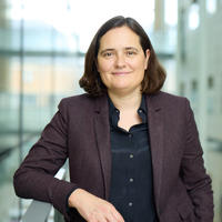 Portrait of Prof Charlotte Williams, a woman with shoulder length brown hair wearing a burgundy jacket and smiling, standing in Oxford's Chemistry Research Laboratory.